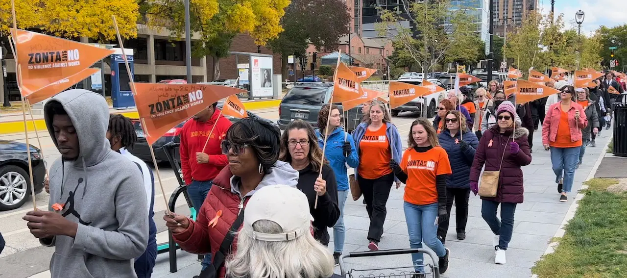 A diverse group of people marching outdoors, many wearing orange shirts and holding signs.