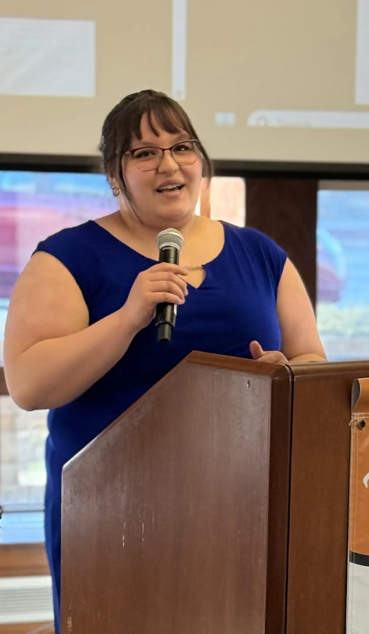 Woman in blue dress speaking at a podium with a microphone.