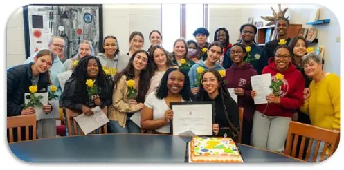 A diverse group celebrating with certificates and flowers indoors.